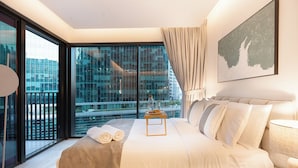 A modern hotel room with a large bed, a view of the city through floor-to-ceiling windows, and a cityscape view from the balcony. - Ahad Residences (Dubai)