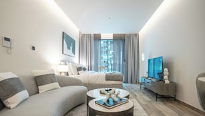 A modern hotel room with a sofa, a small table with a book, a TV, and a large window with curtains. - Ahad Residences (Dubai)