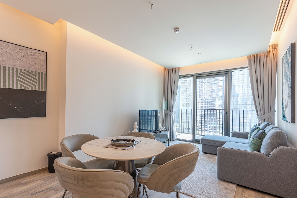 A modern living room with a round table, comfortable seating, a sofa, and large windows offering a city view.