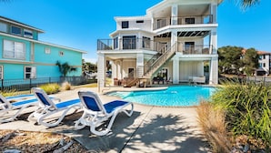 A two-story building with a swimming pool, lounge chairs, and a staircase leading to the upper level. - A Peace of Paradise (Pensacola Beach)