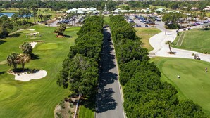 An aerial view of a golf course with a central road, surrounding greenery, and distant buildings. - Studio at the PGA (Port St. Lucie)