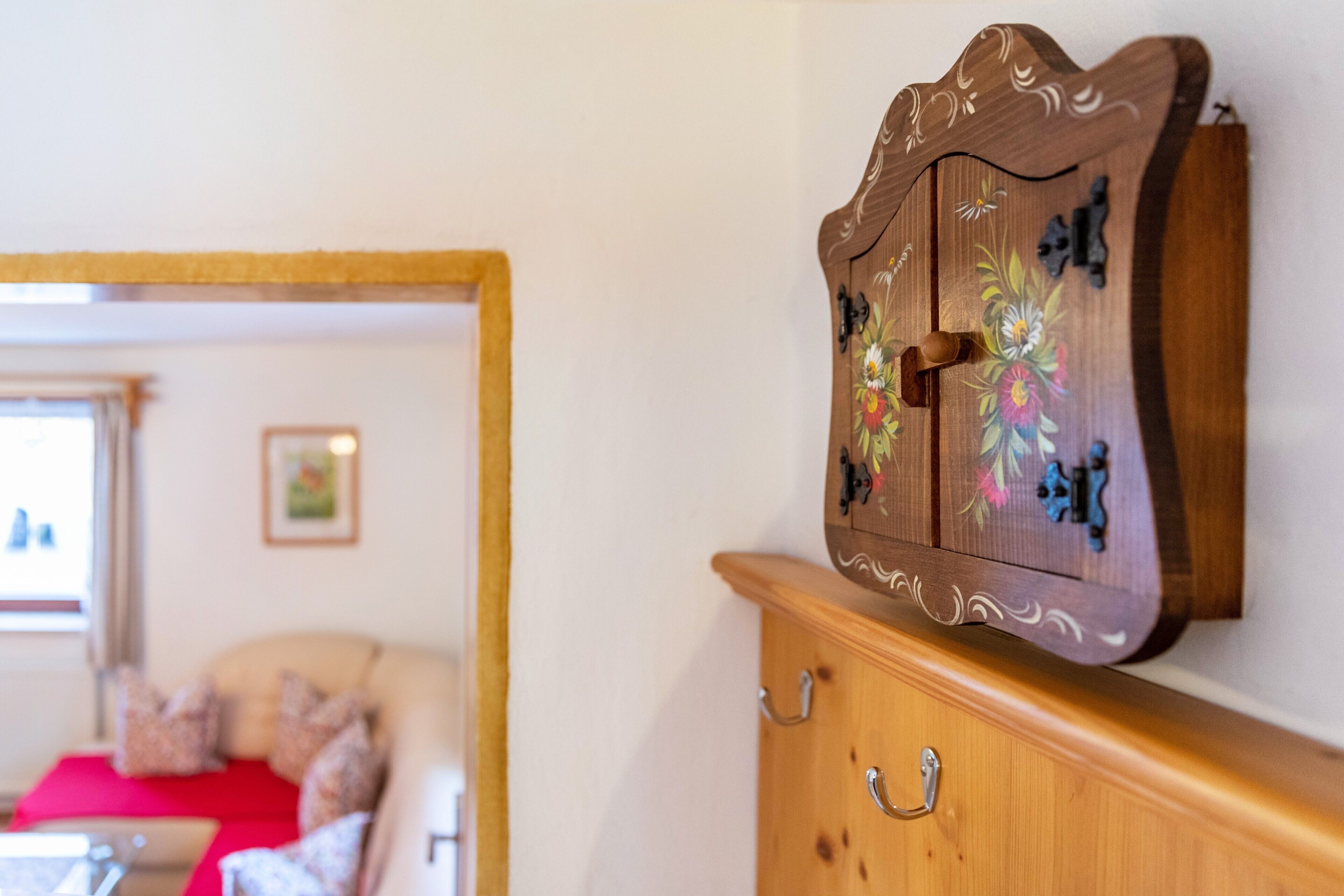 Un meuble en bois orné de motifs floraux, un miroir et un canapé rouge en arrière-plan.