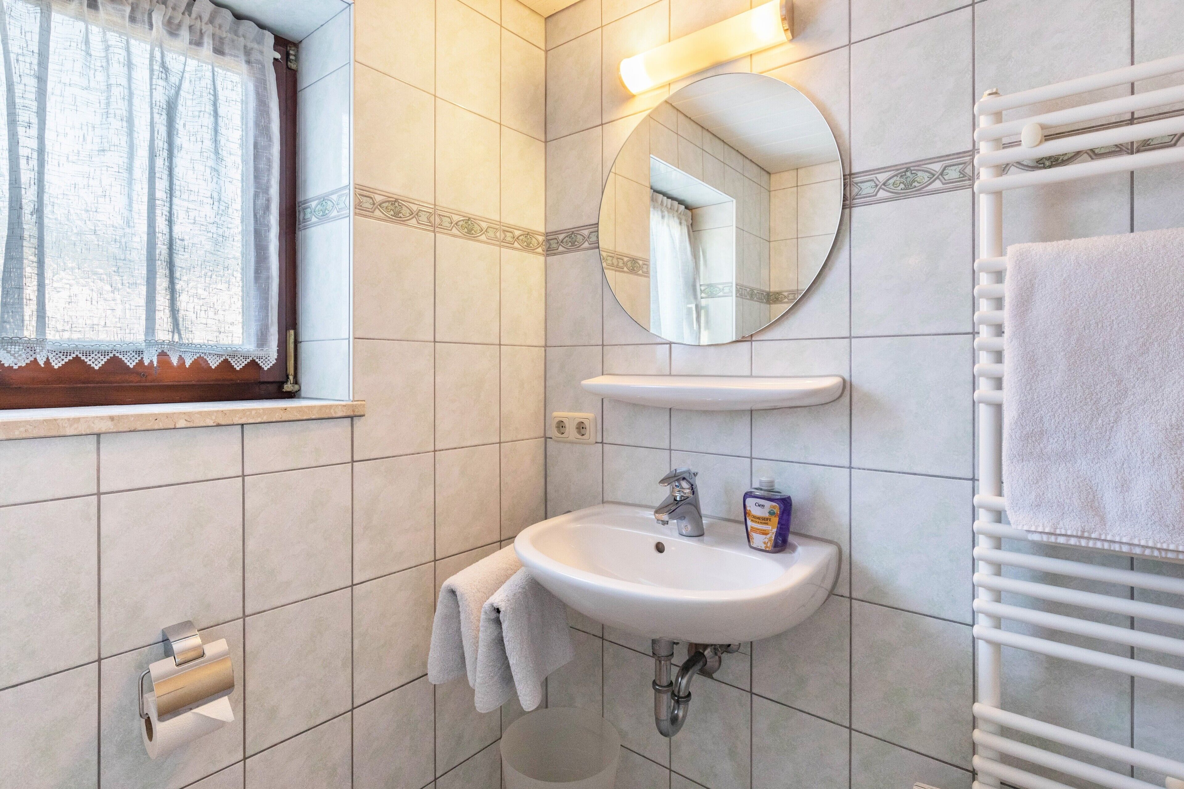 A bathroom with a sink, mirror, towel rack, and toilet paper holder.