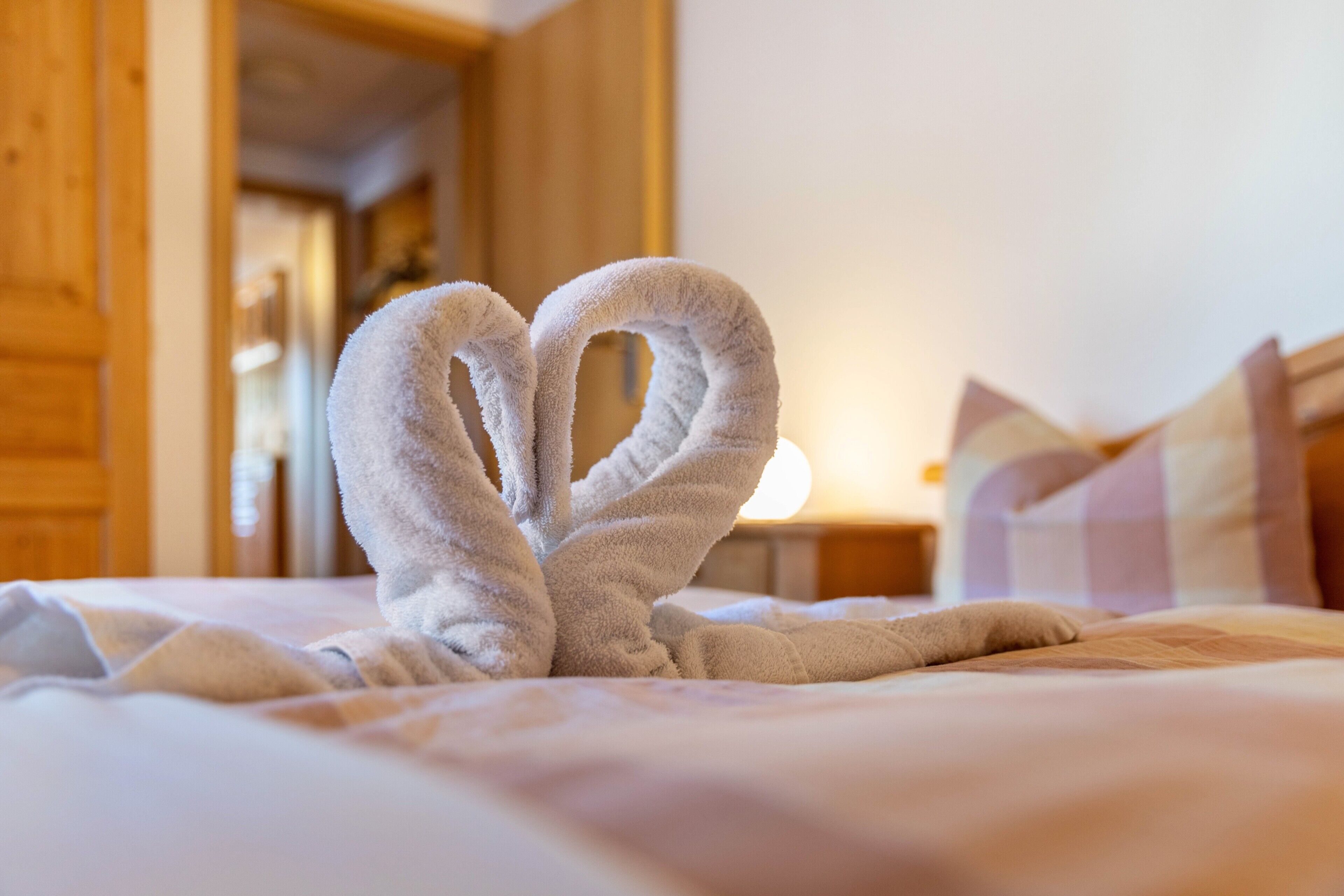 Ein Bett mit einer herzförmigen Handtuchgestaltung, Holzwänden und einem Nachttisch mit Lampe.