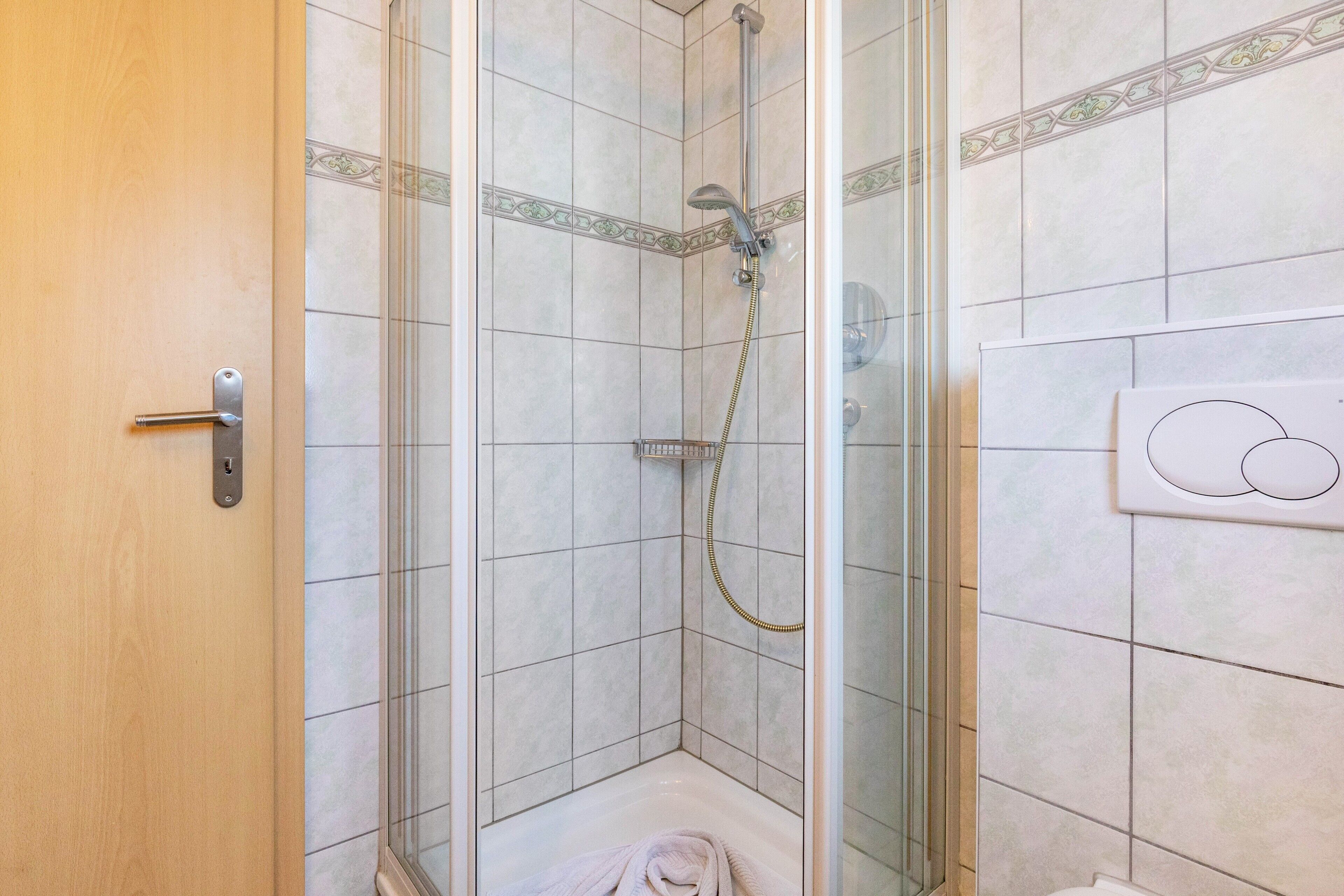 Eine Dusche mit Glastür, ein Handtuch auf dem Boden und eine Toilette mit Bidetfunktion.