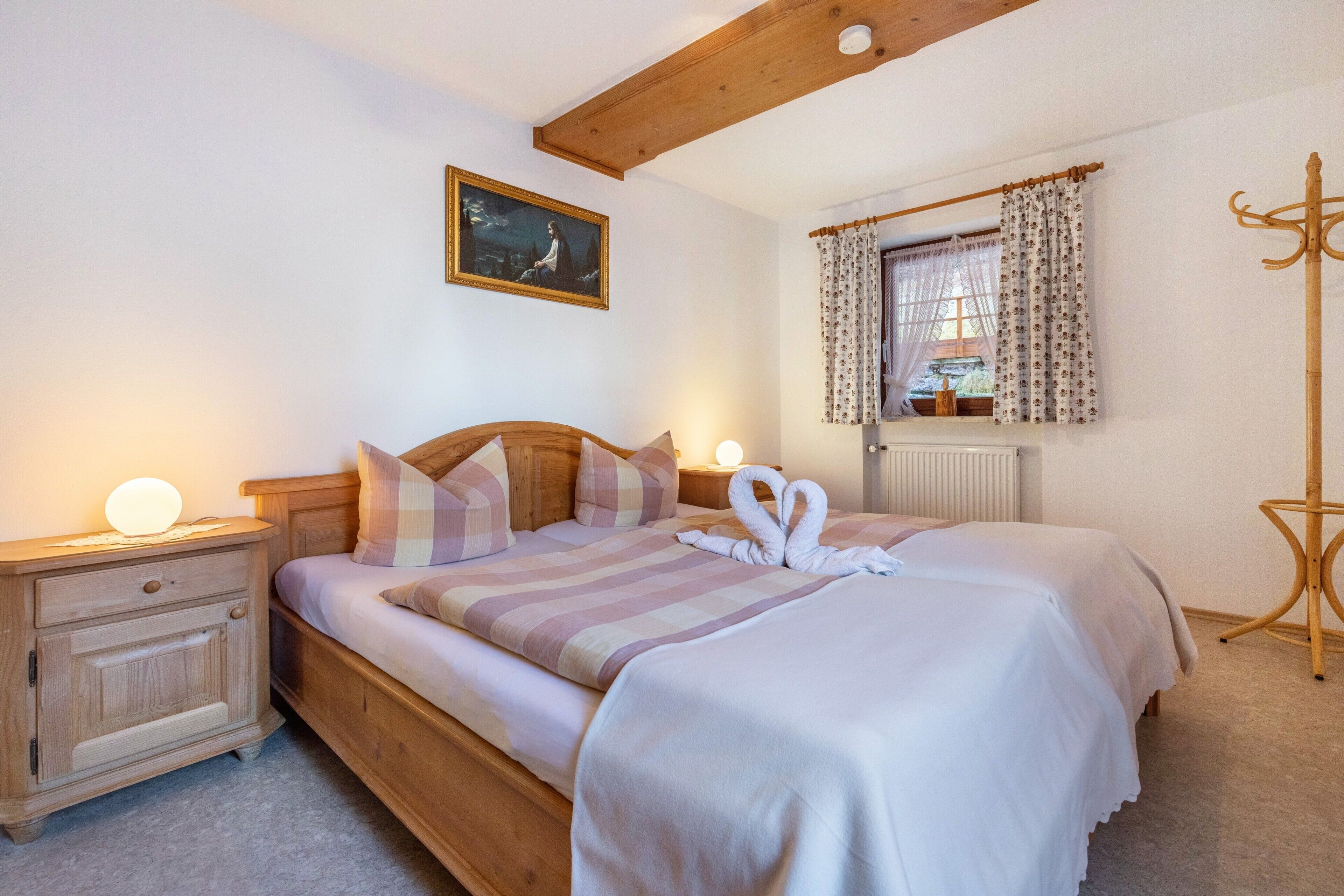 Een slaapkamer met een houten bed, een nachtkastje, een bedlamp, een raam met gordijnen en een kapstok.