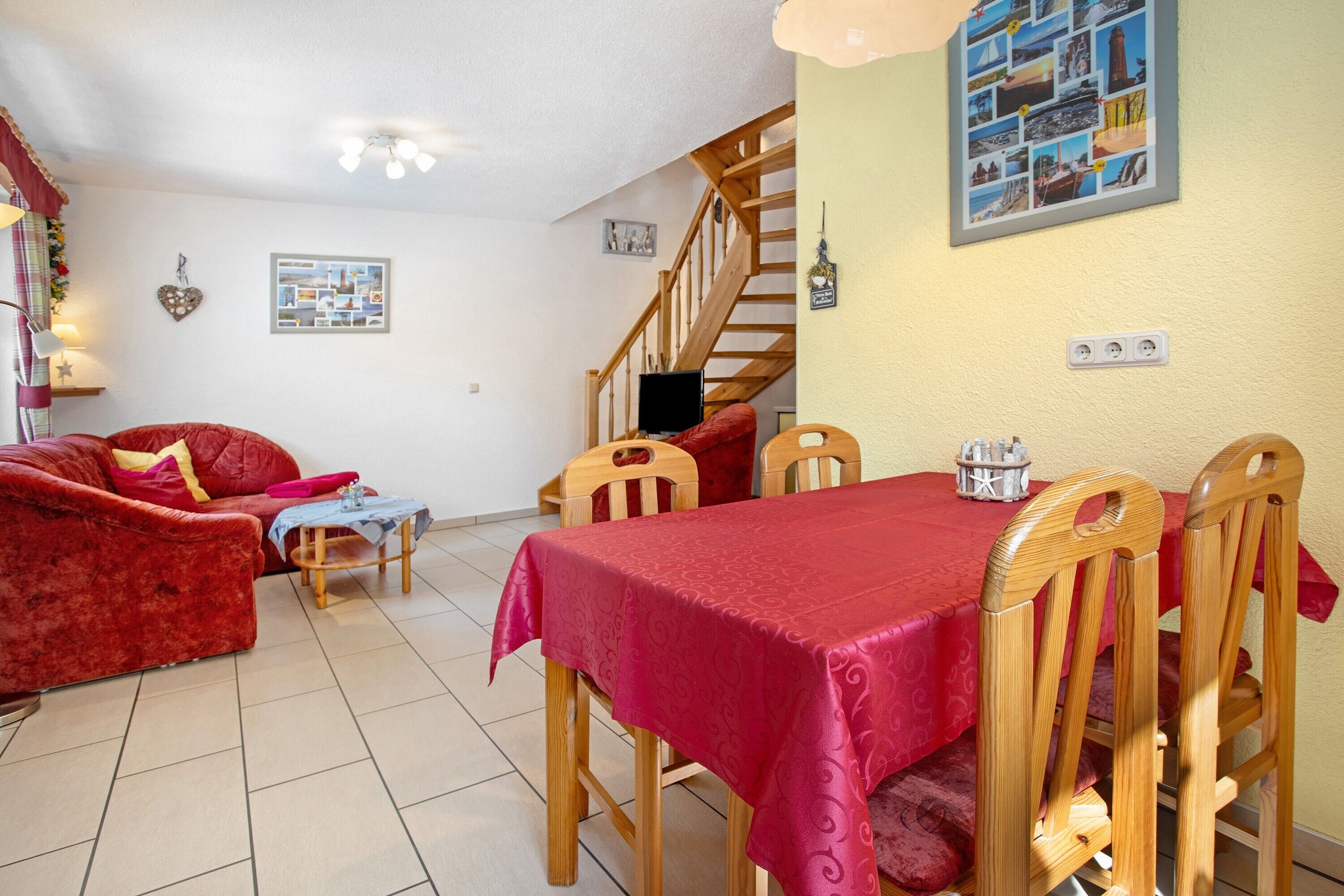 A dining area with a table set for four, wooden chairs, a red tablecloth, and a staircase leading to an upper level.