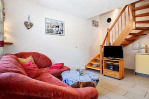 A cozy living room with a red sofa, a coffee machine, and a wooden staircase. - Apartment 'Fewo 11 - Halbinsel Darss - Ostsee' with Private Terrace, Shared Garden and Wi-Fi (Wieck am Darß)