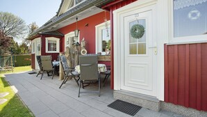 Een rode woning met een witte deur, een veranda met stoelen en een kleine tafel.