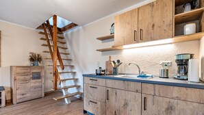 Une cuisine avec des meubles de rangement en bois, un escalier en bois et un plan de travail équipé d’appareils électroménagers.