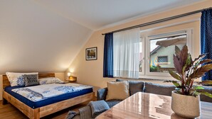Une chambre à coucher avec un lit en bois, un canapé, une table à manger et une vue sur une maison par la fenêtre.