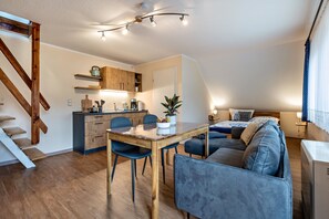 En kompakt opholdsstue med spiseplads, tekøkken og sofa.