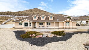 Une maison à deux étages avec un porche à l’avant, une allée et une montagne en arrière-plan.