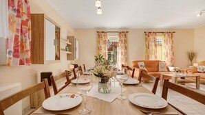 A dining area with a long table set for four, wooden chairs, a vase with flowers, and a view of the living room. - Holiday Home 'Bauernnest' with Shared Garden and Wi-Fi (Schmogrow-Fehrow)