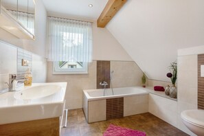 Une salle de bain moderne avec une grande baignoire, un lavabo double et une fenêtre ornée de rideaux légers.