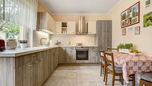 A compact kitchen with wooden cabinets, a built-in oven, and a dining area with a table set for two. - Holiday Home 'Bauernnest' with Shared Garden and Wi-Fi (Schmogrow-Fehrow)