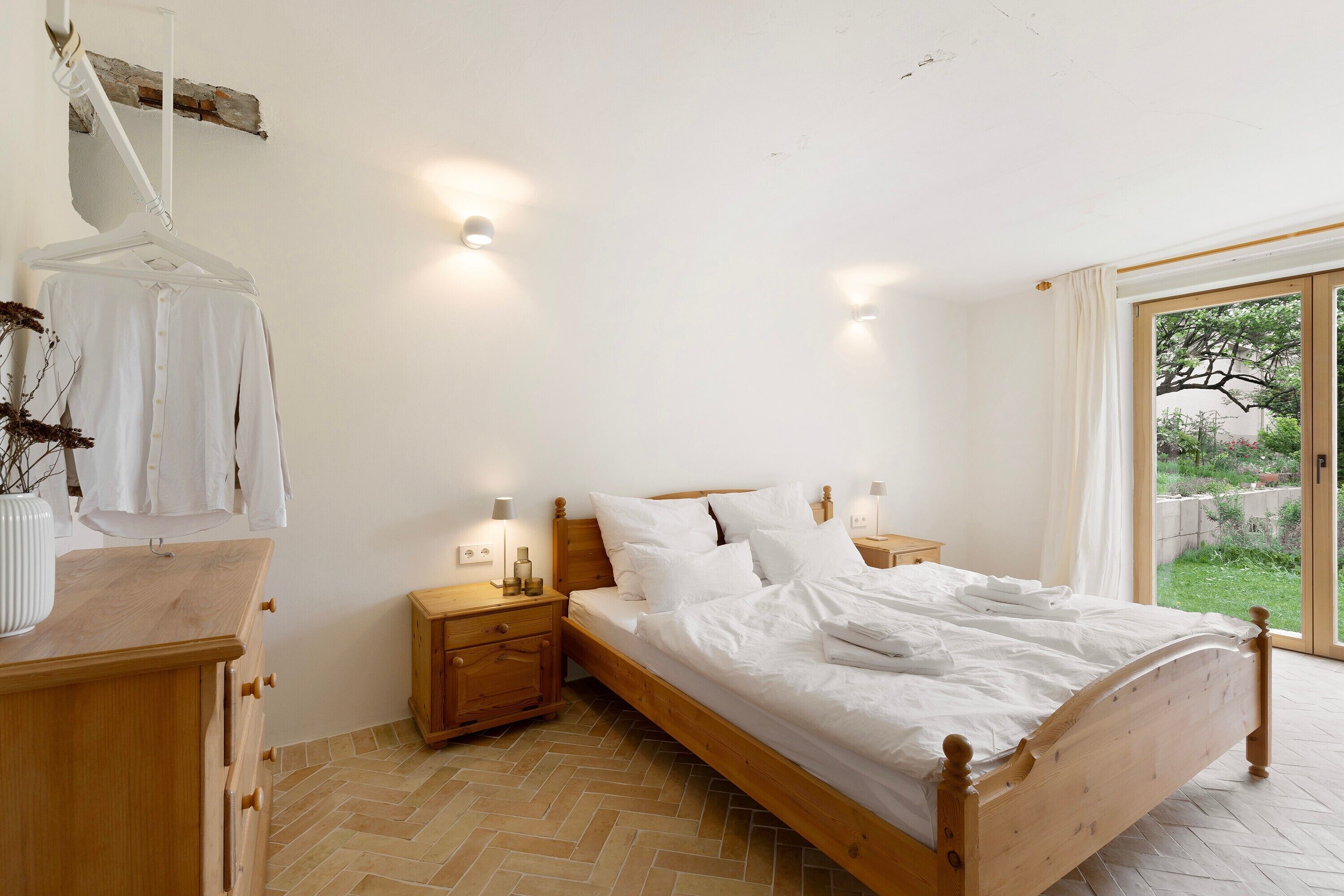 A bedroom with a wooden bed, bedside tables, a hanging robe, and a view through a glass door.