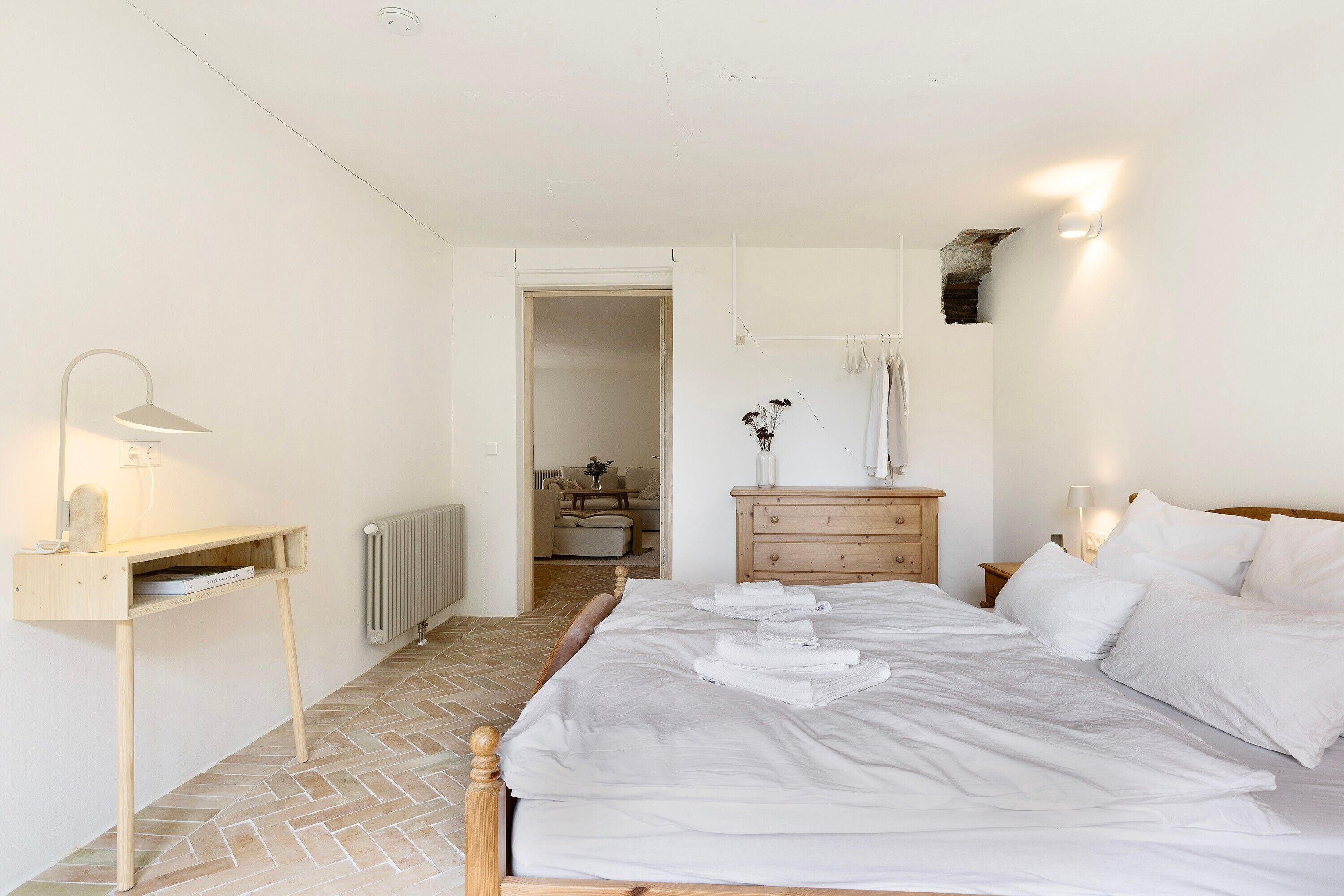 A bedroom with a bed, bedside table, lamp, dresser, and a radiator.