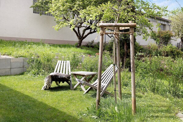 A wooden pergola with ropes, a wooden table, and a bench in a grassy garden area.