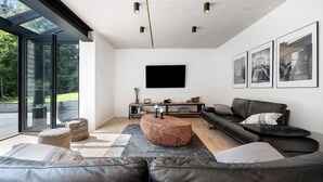 A modern living room with a sofa, ottoman, and a flat-screen TV mounted on the wall.