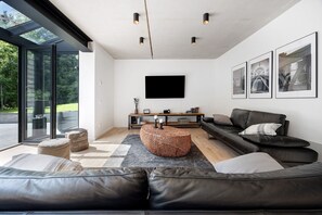 Un salon moderne avec un canapé, un pouf et un téléviseur à écran plat fixé au mur.