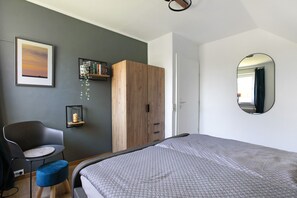 A bedroom with a bed, a chair, a small table, a wardrobe, a framed picture, and a mirror. - Apartment 'Hoern 1' with Wi-Fi (Nordstrand)