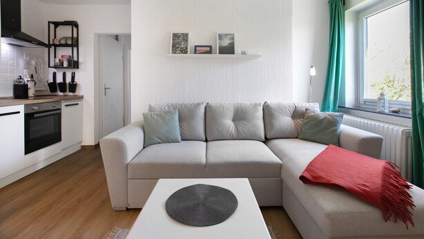 A modern living room with a sofa, a coffee table, and a kitchen area with cabinets and a stove. - Apartment 'Hoern 1' with Wi-Fi (Nordstrand)