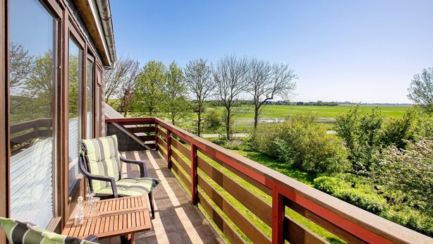 En balkon med et træbord, to stole og udsigt over et grønt landskab.