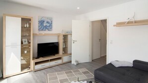 Una sala moderna con televisor de pantalla plana, mueble de entretenimiento de madera, sofá gris y una puerta que da a otra habitación.