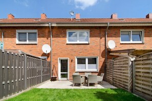 A two-story brick house with satellite dishes, a fenced backyard, and a patio with outdoor furniture.