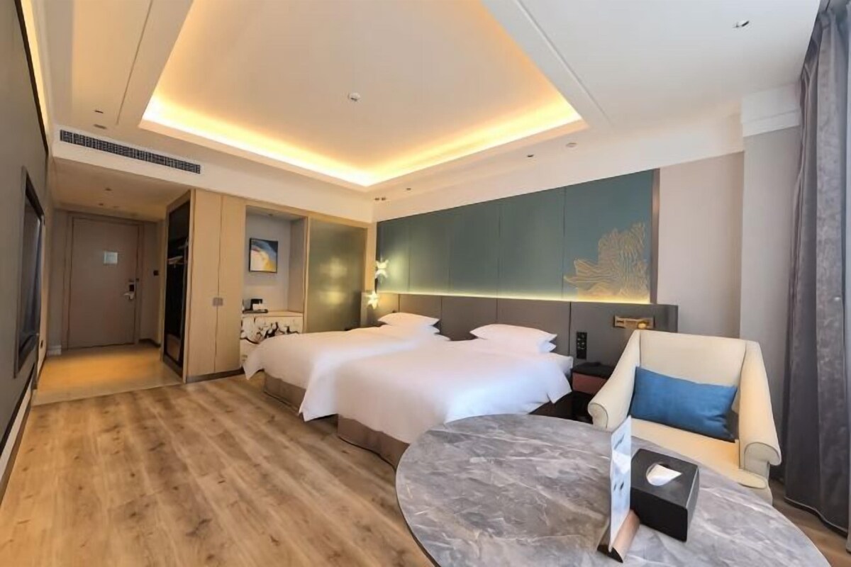 A hotel room with a large bed, a smaller bed, a seating area with a table, and a large artwork on the wall.