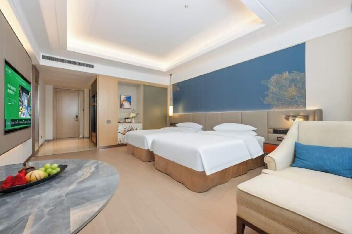 Ein Hotelzimmer mit zwei Betten, einer Schlafcouch, einem Fernseher und einer Obstauswahl.