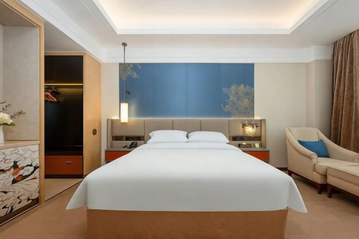 A hotel room with a large bed, bedside tables, a chair, and a wardrobe.