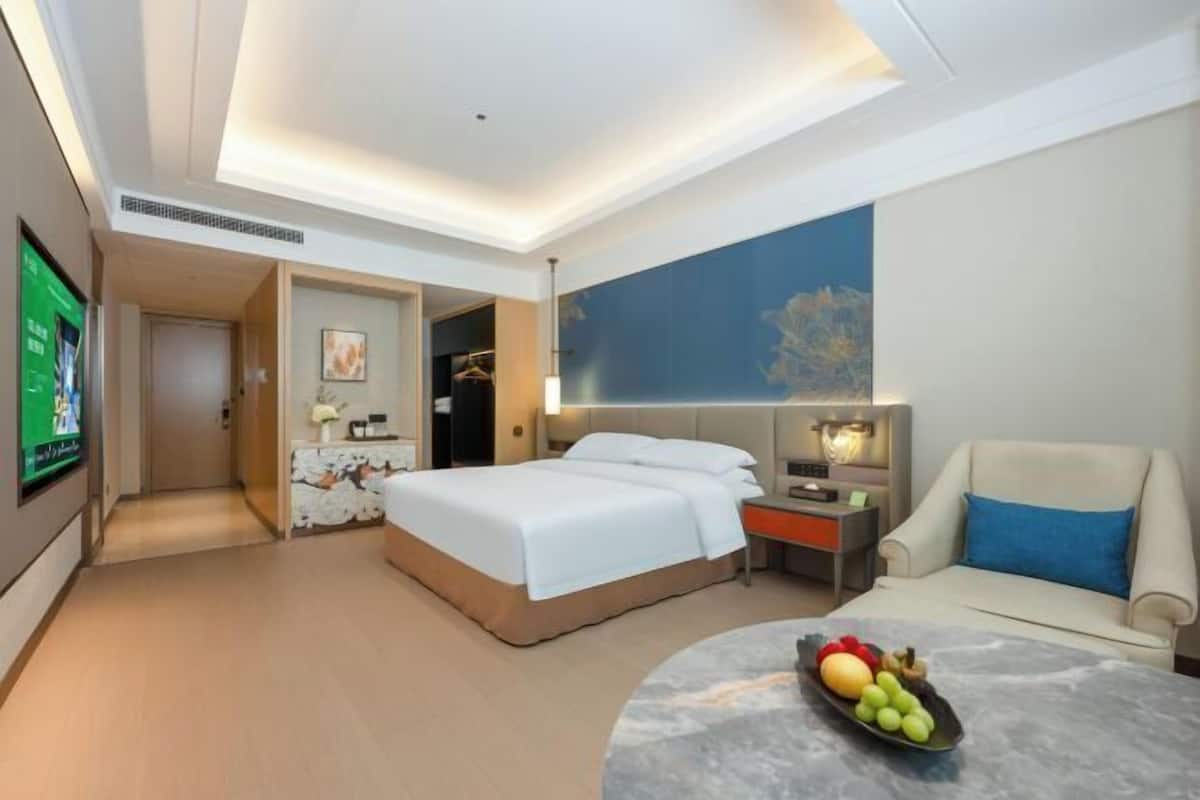 Ein Hotelzimmer mit Bett, Fernseher, Schreibtisch, Stuhl und Obstschale.