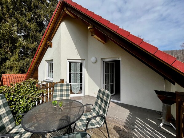 A house with a red roof, a balcony with a table and chairs, and a door.