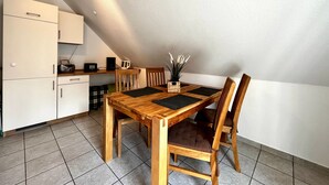 A dining area with a wooden table and chairs, a coffee maker, and a radio on a shelf.
