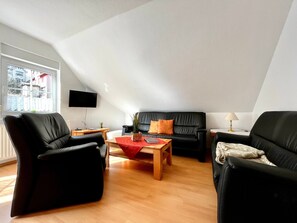 A modern living room with a black leather sofa, a wooden coffee table, and a TV mounted on the wall.
