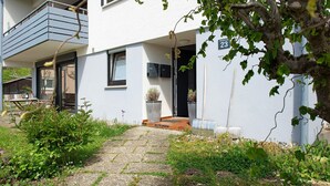 Una casa moderna de dos pisos con entrada pavimentada, plantas en macetas y el número 23 visible en la pared.
