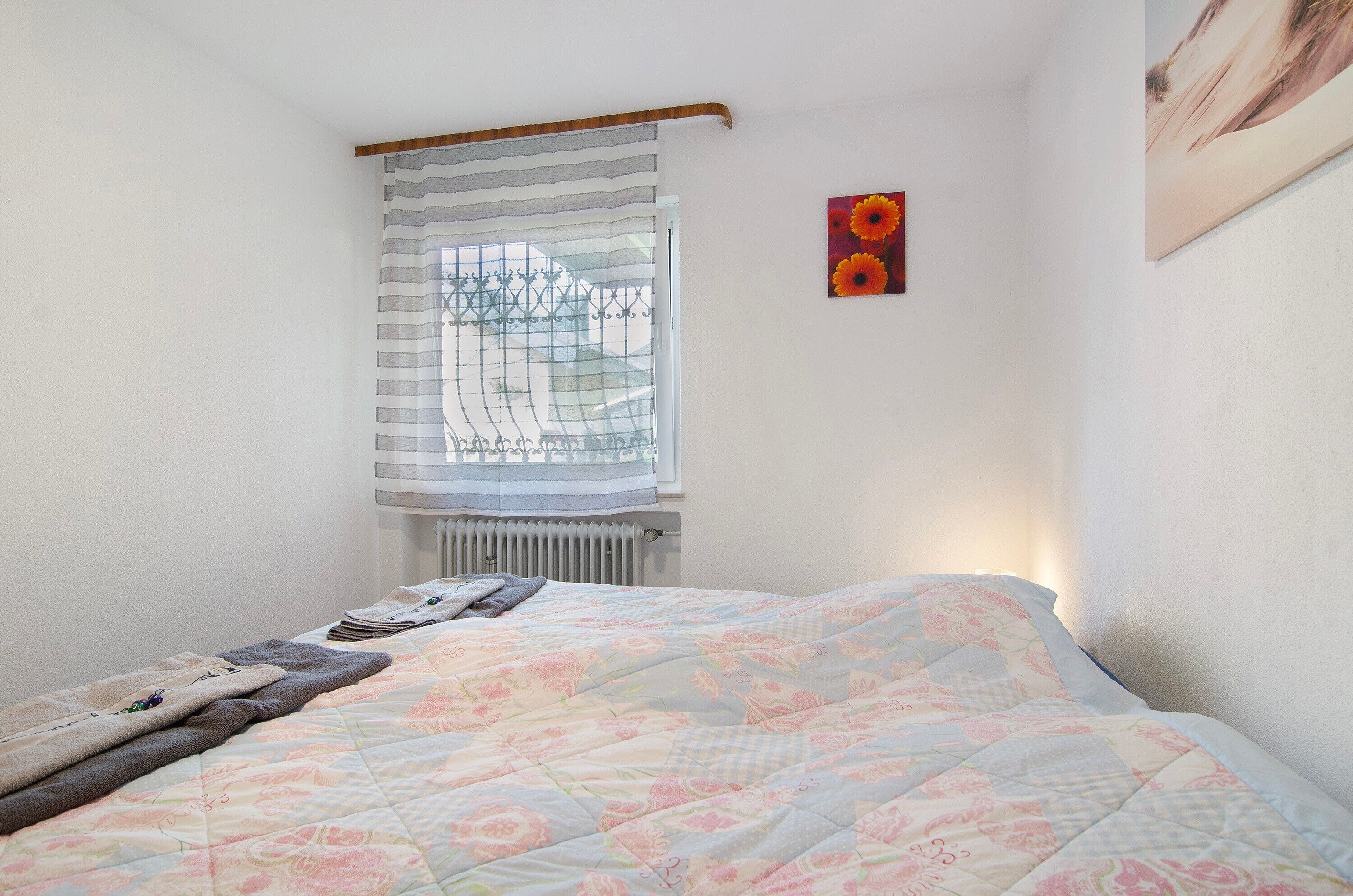 Un dormitorio con cama, un radiador, una ventana con cortinas y un cuadro en la pared.