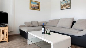 Una sala de estar moderna con un sofá modular, un televisor de pantalla plana, una mesa de centro blanca y dos cuadros enmarcados en la pared.