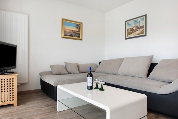 A modern living room with a sectional sofa, a flat-screen TV, a white coffee table, and two framed paintings on the wall.
