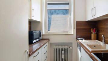 A compact kitchen with a microwave, sink, and window with blinds.
