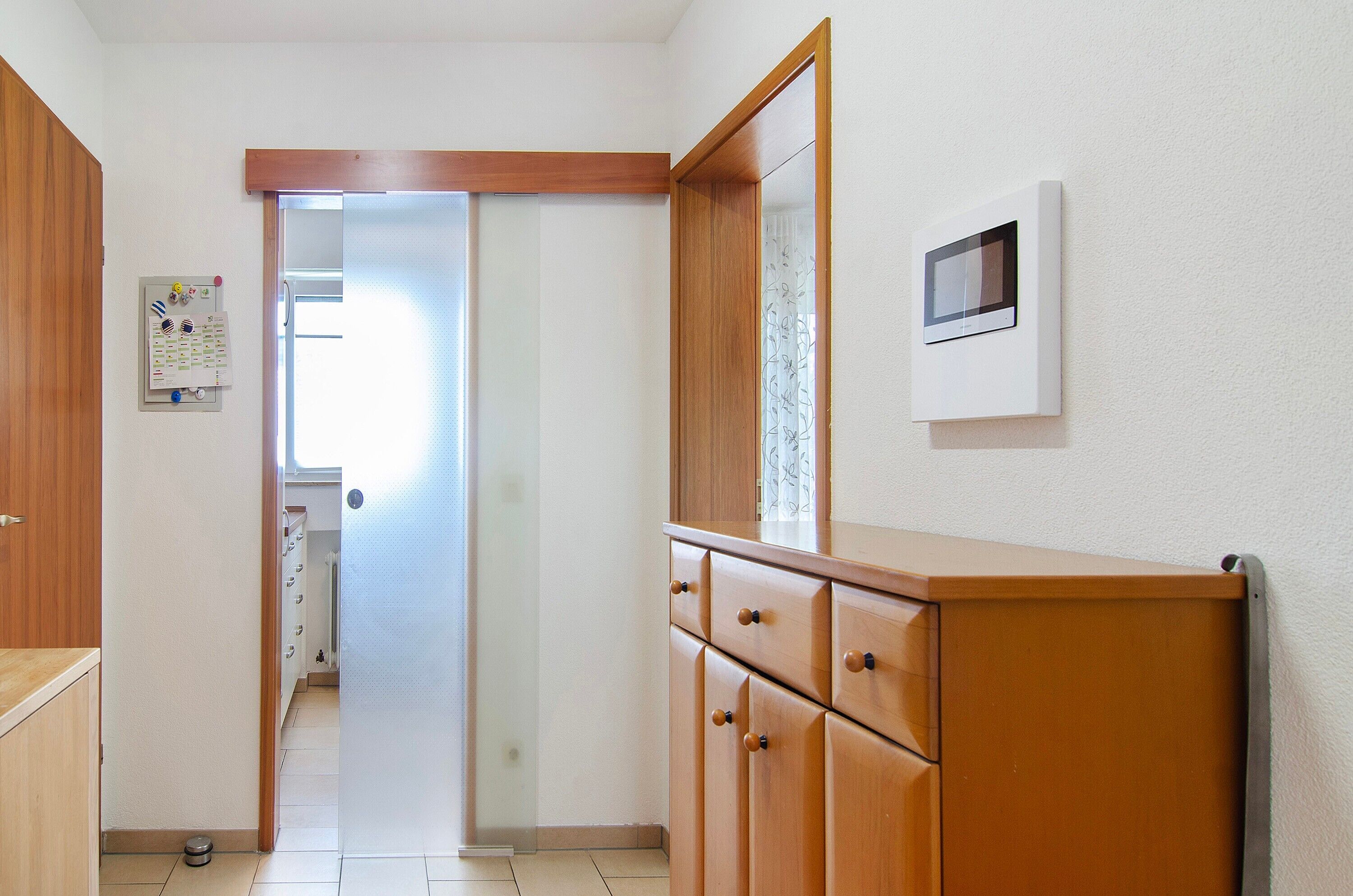 Un couloir avec des armoires en bois, un thermostat et une porte donnant sur une autre pièce.