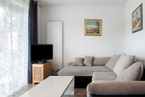 A living room with a sofa, a television on a wooden stand, and a painting on the wall.