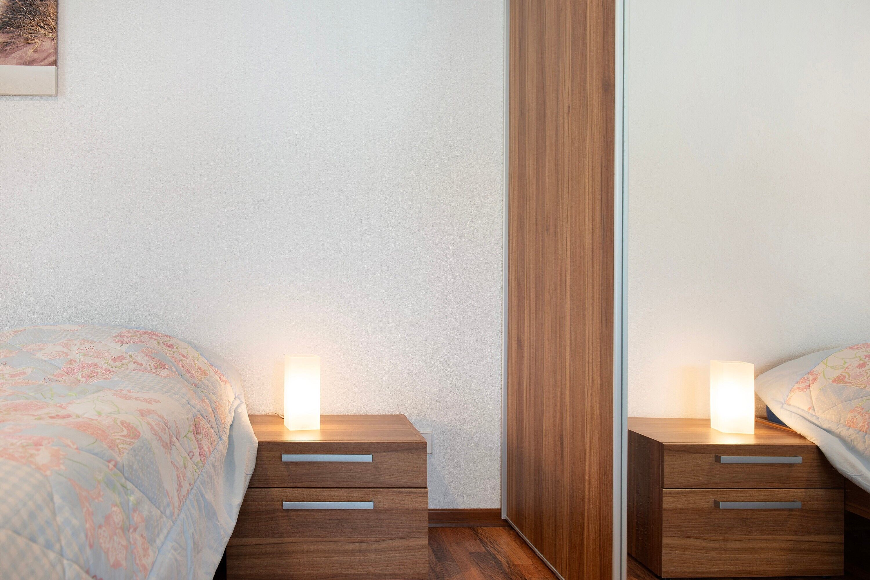 Un dormitorio con una cama, dos mesitas de noche, un armario de madera y un espejo.
