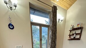 A dining area with a wooden table and chairs, a window with curtains, and a chandelier. - SUNS Cottage (Kasauli)
