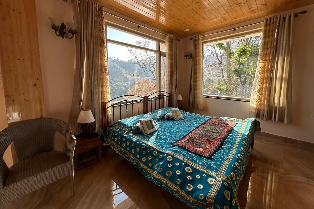 A bedroom with a wooden ceiling, a bed with a patterned bedspread, a chair, and a nightstand with a lamp.