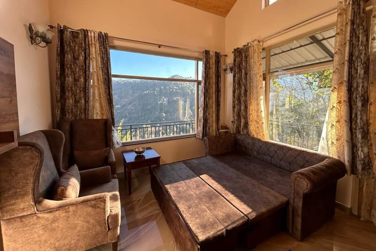 A cozy room with a sofa and armchair, large windows with curtains, and a view of a mountainous landscape.