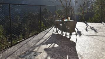 A terrace with a patterned floor, a table with chairs, and a view through a chain-link fence.