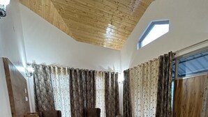 A spacious living room with a high ceiling, a large window, and a modern design. - SUNS Cottage (Kasauli)